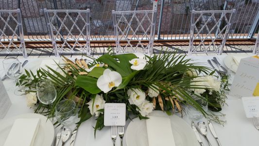 Elongated wedding centerpiece, Bazaar Eclectica Café and Restaurant, Budapest(phalaenopsis orchid, lisianthus, monstera leaf, palm leaf, white, green, gold)