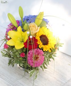 Rainbow colored table decoration in a glass cube (hydrangea, sunflower, rose, lily)