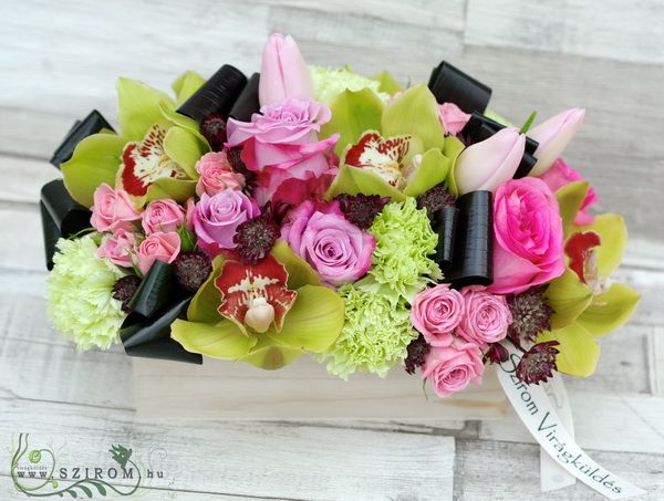 Modern arrangement in wooden box from pink and purple roses, green orchids, tulips, carnations