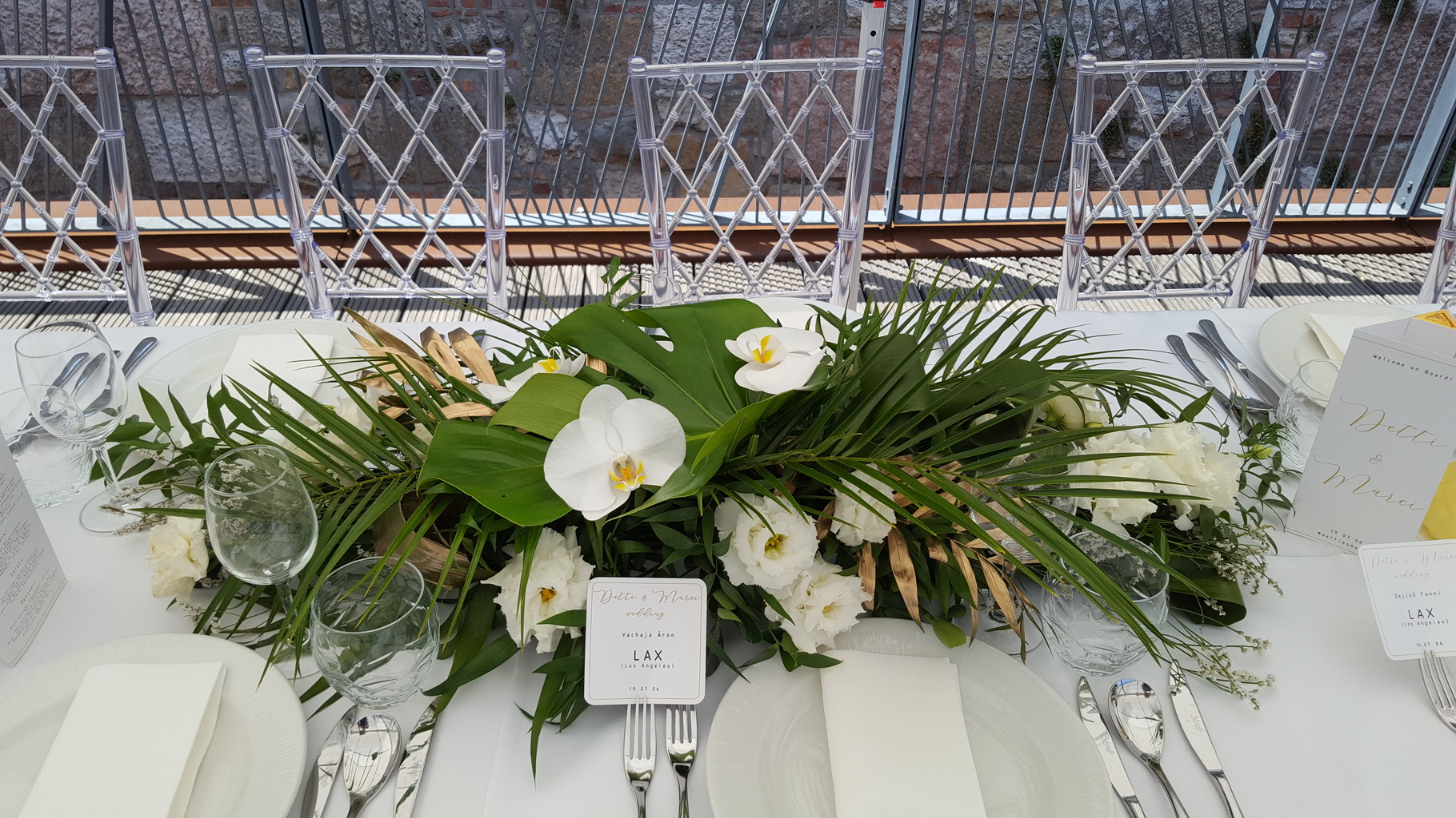 Hosszúkás esküvői asztaldísz, Bazaar Eclektica Étterem, Budapest (phalaenopsis orhidea, lizianthus, monstera, pálmalevél, fehér, zöld, arany)